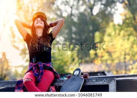 Cute smiling urban girl sitting on skateboard ramp in skate-park