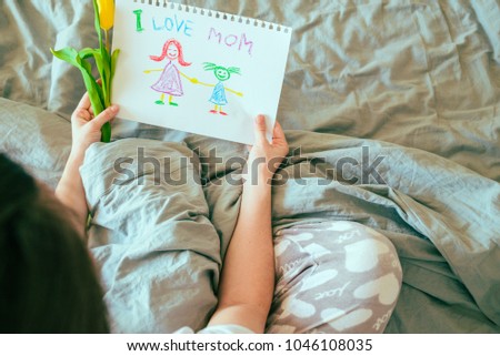 woman sit in bed and look at picture that kids drew for mother day