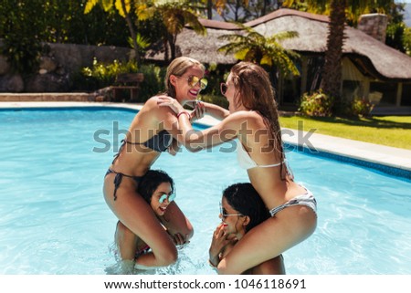 Women sitting on their friends shoulders fighting and wrestling in pool. Group of female friends enjoying themselves in a swimming pool.