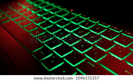 Gamer keyboard with green backlight and red light, focused on a latin symbol.