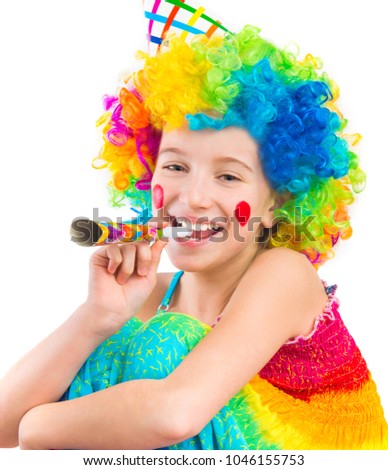 Cheerful young little girl in curly clown wig and party horn blower isolated on white background