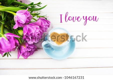A cup of cappuccino with a heart shaped symbol and purple tulips on a wooden background-inscription I love you.