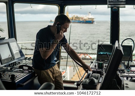 Deck navigation officer on the navigation bridge. He speaks by VHF radio, GMDSS Watchkeeping, collision prevention at sea. COLREG Royalty-Free Stock Photo #1046172712