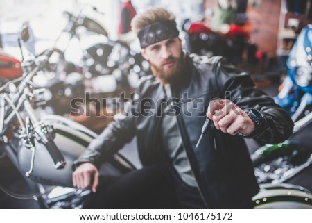 Handsome bearded man in motorcycle shop. Biker is choosing new vehicle and motorcycle accessories. Holding keys.