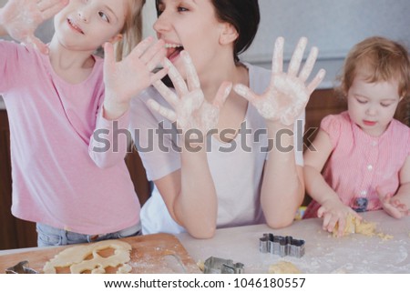 Cute little girls and her beautiful mother are sprinkling the dough with flour and smiling while