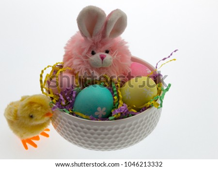 Pink Easter bunny in a white ceramic bowl filled with coloured paper shred and hand dyed eggs. Toy yellow chick at left side of bowl, isolated on white.