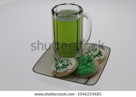 Green beer in glass beer stein with three shortbread cookies, with icing and sprinkles, on a square plate. A toast to St. Patrick’s Day.