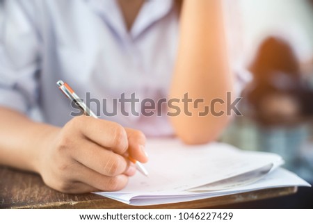 Students writing pen in hand doing exams answer sheets exercises in classroom with stress.