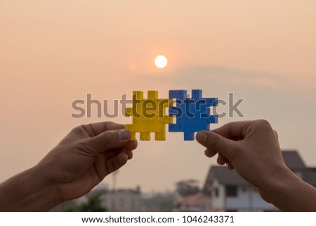 Two hands try to connect the puzzle pieces along with the sun ba