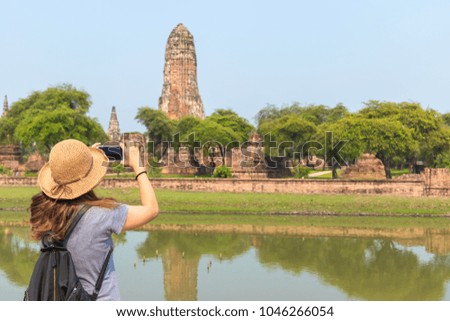 woman traveler with backpack and hat and take a photo with smartphone at (Wat Pharam) temple background from Ayutthaya near Bangkok Thailand. Traveling Thailand, Asia.