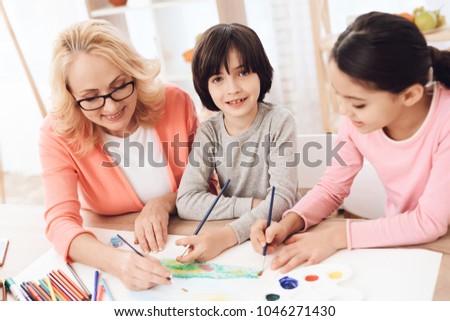 Beautiful elderly woman teaches children to draw. Little children draw. Drawing lessons. Grandmother teaches children to paint with watercolor. Drawing with paints.