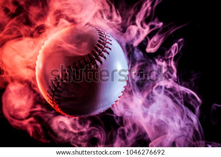 Colorful baseball ball in multi-colored red smoke from a vape on a black isolated background