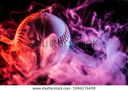 Close up of a white baseball ball in multi-colored red smoke from a vape on a black isolated background