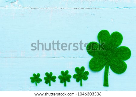 Happy St Patricks Day message and a lot of green paper clover leaf on Pastel white and blue wooden table background texture.