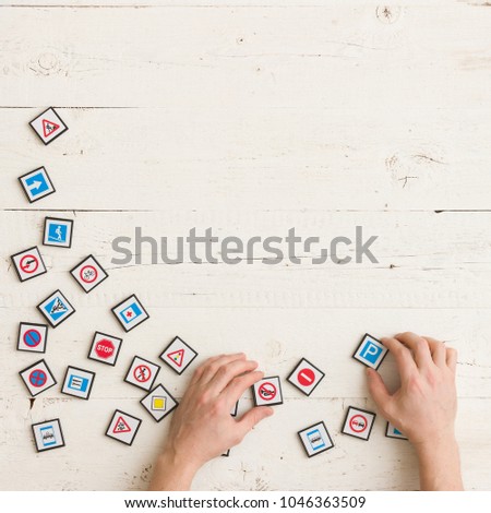 Top view on man's hands playing with toy road signs on white wooden table background.