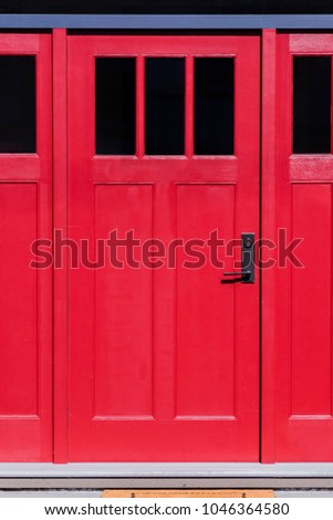 entrance, red, wooden door with black glass windows, a wreath of real flowers and leaves, a metal handle and a bouquet