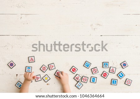 Top view on child's hands playing with toy road signs on white wooden table background. Learning traffic signs.