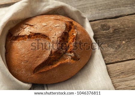 Fresh round rye bread with towel on a wooden table, close-up