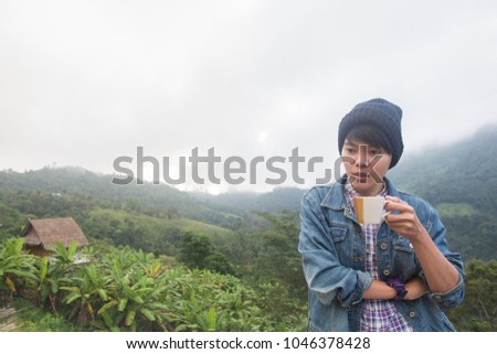 Asian man in Jean jacket And wear black hat,Are smiling holding cup of hot coffee in morning winter season on Mountain Doi Luang Chiang Dao Chiang Mai Thailand