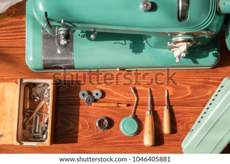 an old electric sewing machine with a box with tools and sprinkled coils with threads stands on a wooden lacquered table