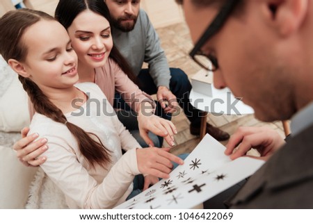 Little girl with her parents goes through logical test with psychologist, choosing figures on sheet. Family of three visit to psychologist. Family psychotherapy concept.
