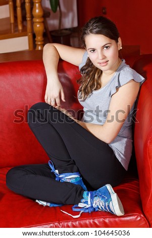 Portrait of a beautiful teenage girl with long brown hair, sitting on red sofa at home, smiling into camera