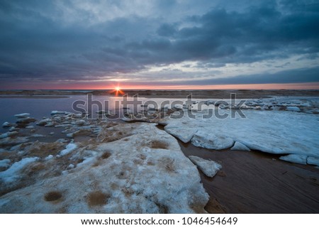Snow and ice melting on sand beach at coast of sea water and spring evening sunset sky clouds light reflection