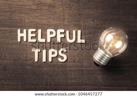 Helpful Tips text with glowing light bulb on wood texture Royalty-Free Stock Photo #1046457277