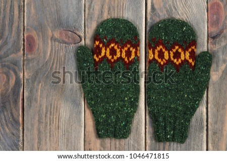 Green knitted mittens handmade on a wooden background. View from above.