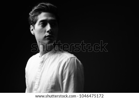 Studio shot of young multi-ethnic handsome man against black background in black and white