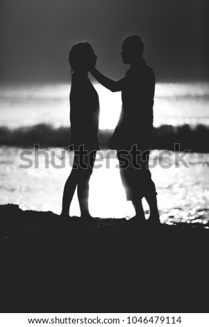 Silhouettes of a loving couple enjoying sunset on the ocean beach. Black and white.