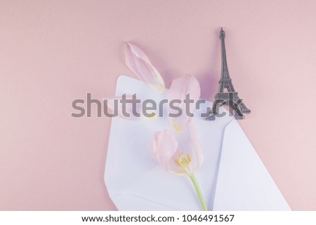 Pink tulip with petals in opened paper envelope letter with eiffel tower miniature on a pink background. Flat lay top view. Romantic love memories concept