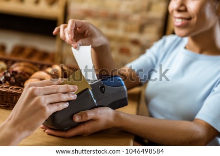 close-up shot of smiling cashier with pos terminal receiving purchase from client at pastry store