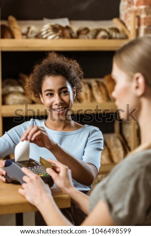 young cashier with pos terminal receiving purchase from client at pastry store