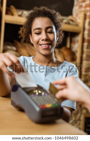 close-up shot of happy cashier with pos terminal receiving purchase from client at pastry store