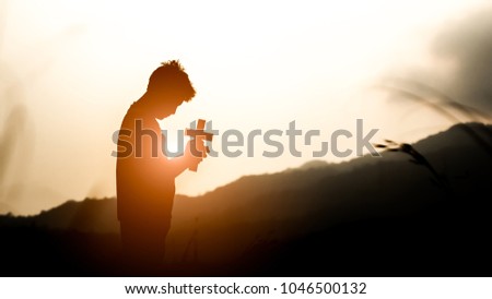 Young holding christian cross with light sunset background