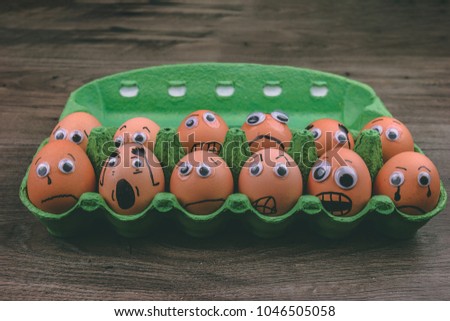 Fun concept: raw eggs with googly eyes and drawn features are in shock and sad while they sit in a green carton box on top of a wooden table