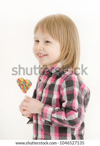 Portrait of a happy and emotional pretty little girl with blond hair and a plaid shirt, gazing with a smile on his face in the mirror holding a sweet candies on a stick isolated on a white background