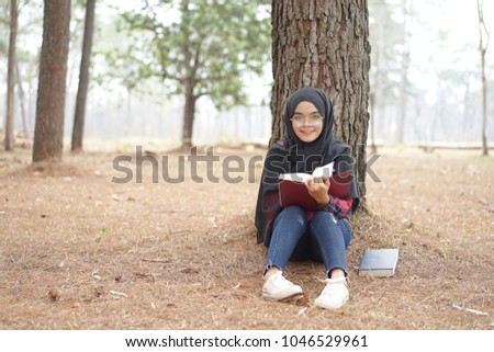 Portrait of happy young muslim woman black hijab and Scottish shirt reading a book in autumn season  background.