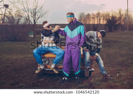 Three friends in the style of the nineties are about orange old car Royalty-Free Stock Photo #1046542120