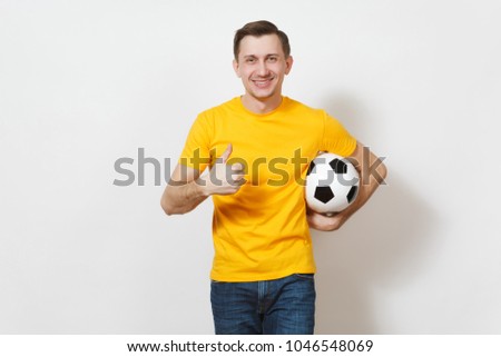 Inspired young European man, fan or player in yellow uniform hold soccer ball, show thumb up, cheer favorite football team isolated on white background. Sport play football, healthy lifestyle concept