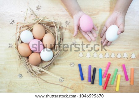 Many white, pink and orange eggs are in the straw basket and put on the wooden table with many colorful pens and kids hands. The picture concepts are food, healthy, Easter, family.