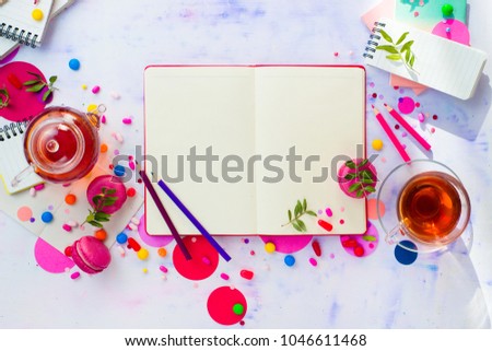 Feminine writer workplace with an open notepad or diary. Colorful sweet snacks, hard candy, and pink macarons on a light wooden background with copy space.