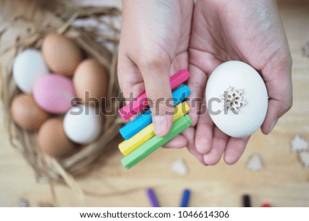 Her hands are holding the white egg and many colorful pens with the wooden table background. The background has many eggs are in the straw basket. The picture concepts are food, healthy, Easter.