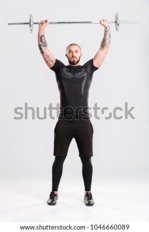 Full lenght picture of strong healthy young sportsman. Looking camera make sports exercises with barbell.