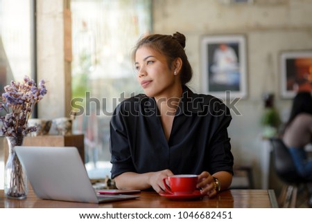 Asian woman working in cafe and looking out window.