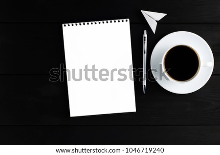 open notepad, pen, paper airplane, white mug with black coffee