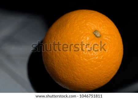 A photo of an orange on a black and white background with slight reflection and light coming from above, great for posters, media and commercial use.   