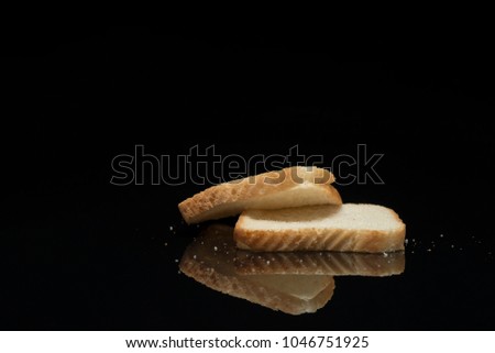 A perfect photo of two slices of white bread with bread crumbs on a black organic glass positioned great for posters, media and commercial use. 