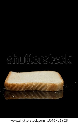 A perfect photo of a slice of white bread laying down with bread crumbs on a black organic glass positioned great for posters, media and commercial use. 